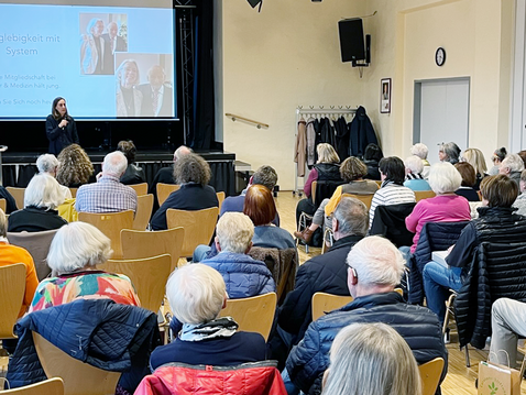 Blick auf Rückenansicht eines Publikums in Kettwig, vorne die Referentin Claudia Wendt. 