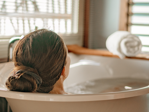 Rückansicht einer langhaarigen Person mit dunkelblondem Haar, die entspannt in einer freistehenden Badewanne liegt.