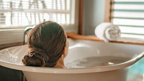 Rückansicht einer langhaarigen Person mit dunkelblondem Haar, die entspannt in einer freistehenden Badewanne liegt.